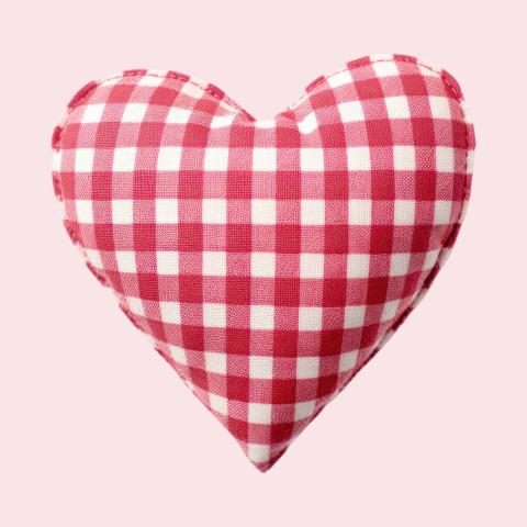 Image of a heart shaped pillow on a pink background. 