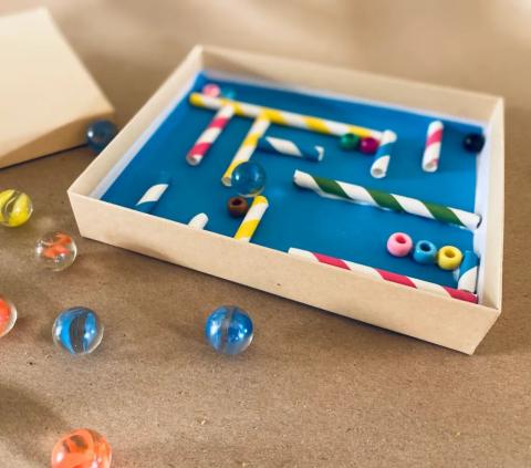 Image of a cardboard box with beads and straws used to create a maze.