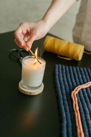 A hand holding a lit match lighting a candle in a glass jar.