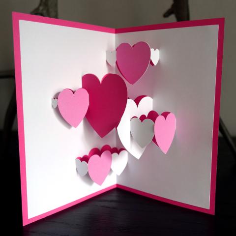 Image of a white and pink Valentine pop up card with multicolored hearts. 