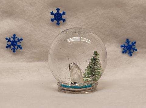 Round jar snow globe with a penguin, a pine tree, and falling glitter inside