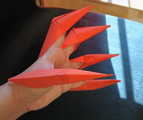 Orange origami paper claws being used on a hand