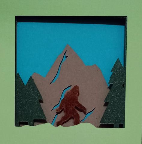 Colorful paper layered and cut out to make a Sasquatch in forest scene
