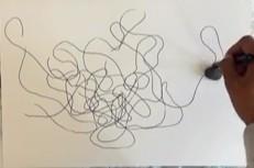 A Black woman's hand is holding a marker behind a small stone on a white piece of paper. The paper is covered in black squiggles and loops.