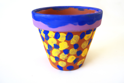 Terra cotta pot with yellow and blue dots on body and purple and blue edge