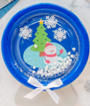 blue paper plate snow globe with a snowman winter scene.