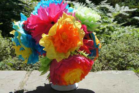 rainbow tissue paper carnations in a vase on top a stone wall
